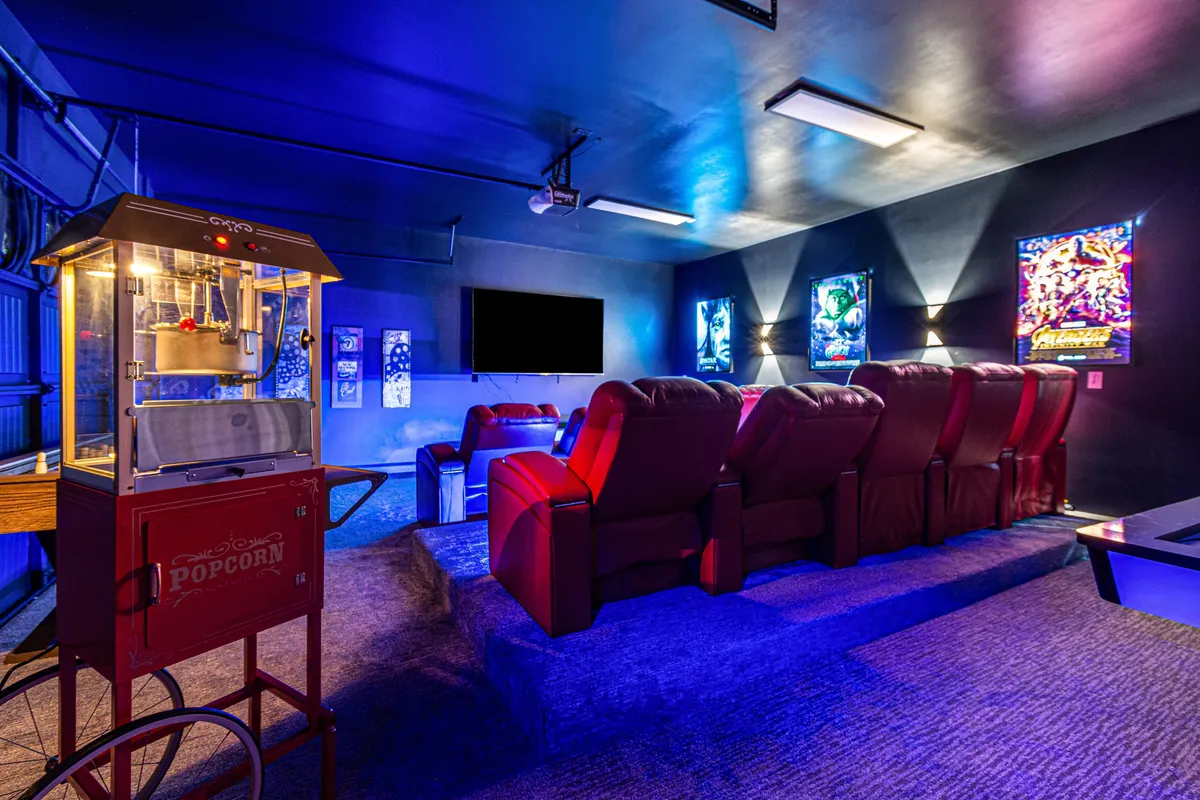 A dedicated home theater with luxurious red reclining chairs arranged in rows, a popcorn machine, a large projector screen, and themed movie posters decorating the walls. The scene feels entertaining and relaxed, capturing the essence of a private movie night or group film screening.