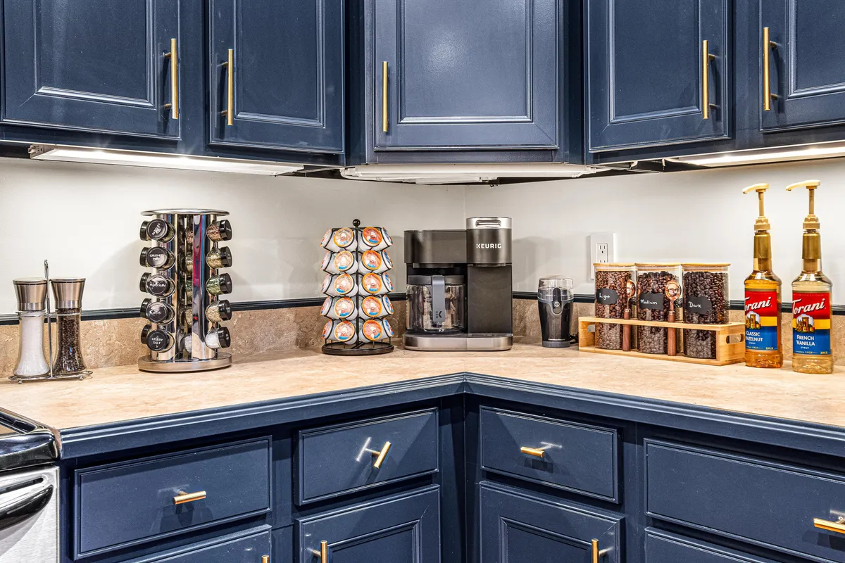 A dedicated coffee bar with stylish blue cabinetry, a coffee maker, syrup dispensers, and neatly organized canisters. The space is both cozy and functional, inviting casual conversation and morning rituals.