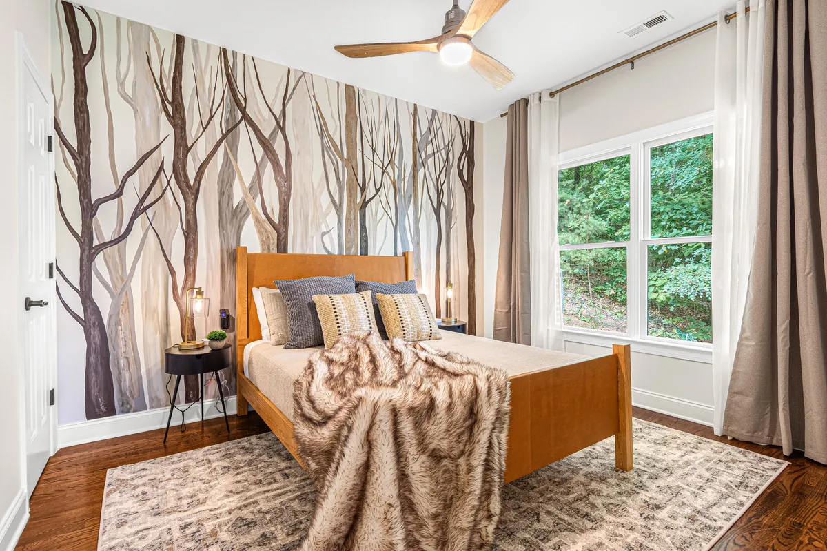 A serene bedroom featuring a bed with a cozy throw blanket, a nature-inspired tree mural on the wall, and a bedside table with a soft-lit lamp. The overall mood is relaxing and tranquil, providing a sense of retreat and comfort ideal for restful sleep.