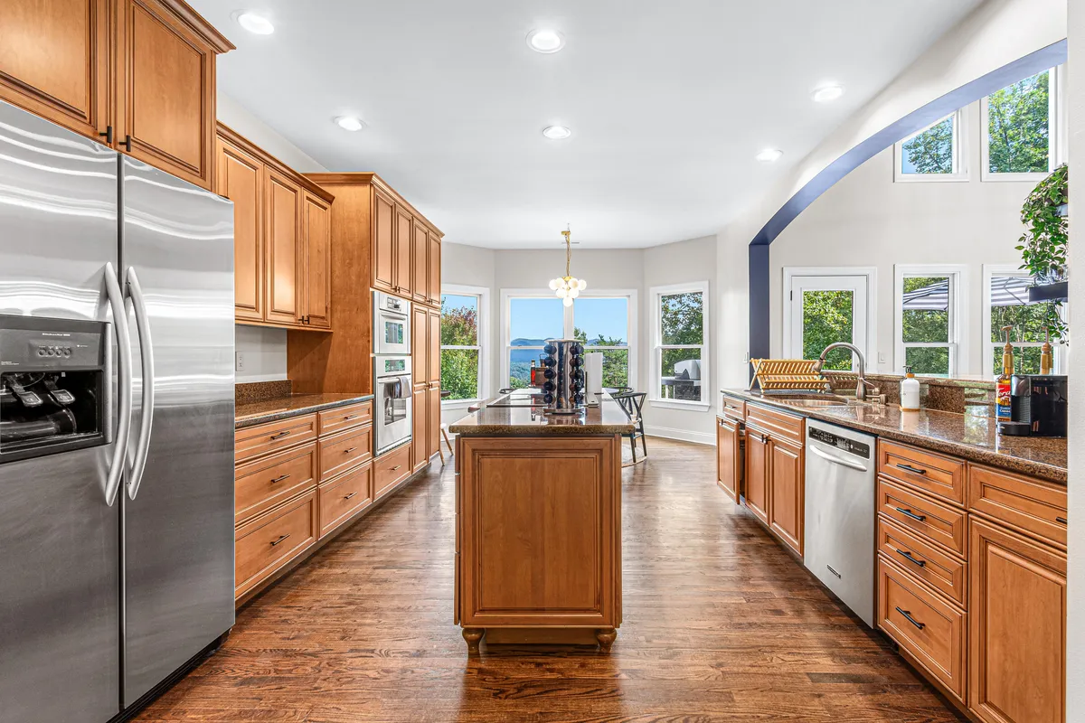 A modern, gourmet kitchen featuring a spacious island, stainless steel appliances, and plenty of natural light streaming through large windows. The space is designed for cooking together, socializing, and enjoying the view while prepping meals or coffee.