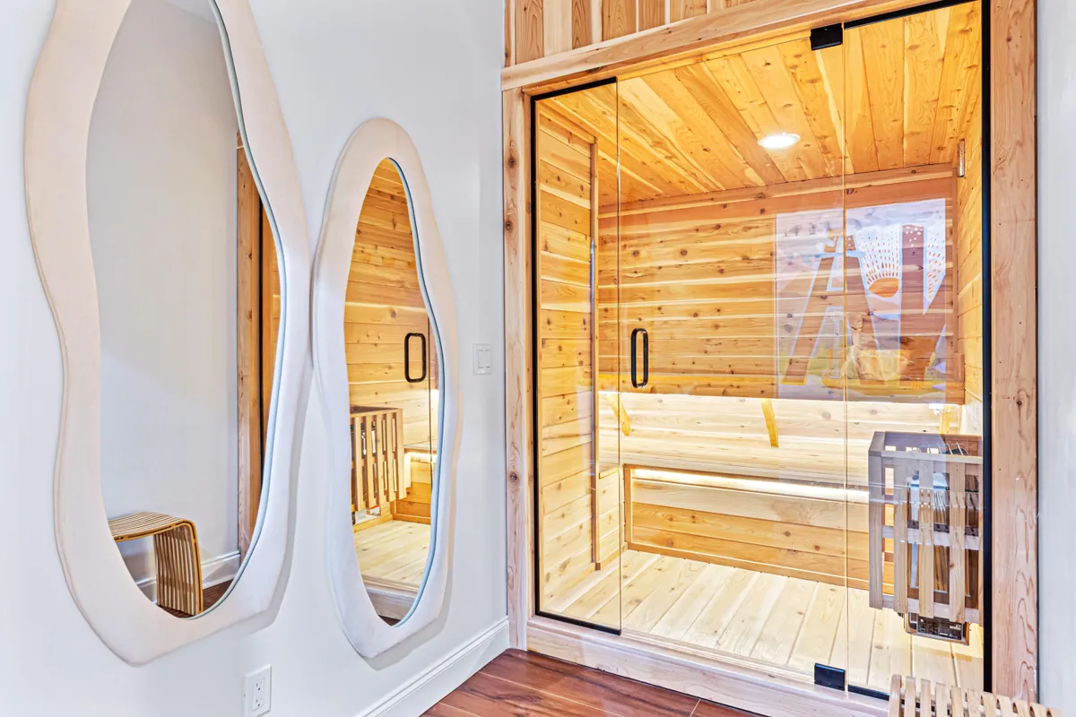 This image features a tranquil custom sauna with inviting wooden textures, mirrored walls, and gentle lighting, creating an ideal environment for relaxation and post-workout recovery. The serene interior hints at a spa-like ambiance that supports moments of self-care and wellness.