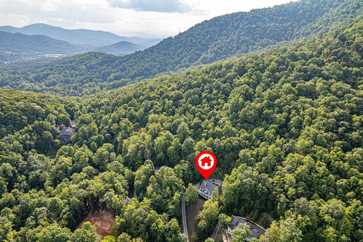 This image presents the house nestled among lush trees with surrounding mountains in the background and a winding road leading to the property. It evokes a peaceful, nature-immersed setting ideal for outdoor adventures.