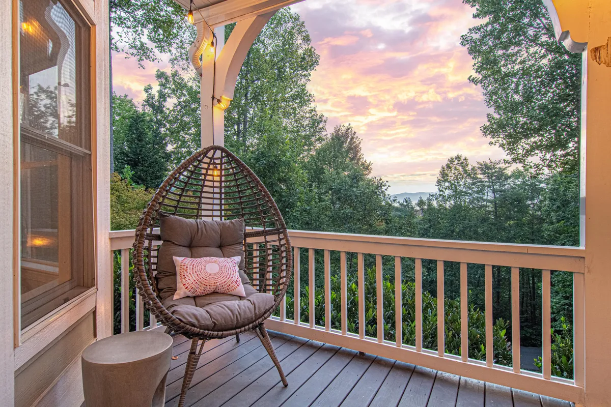 A serene outdoor deck featuring a hanging chair and wooden railing overlooking a scenic sunset view. The ambiance is peaceful, inviting guests to relax, read, or simply take in the mountain surroundings.
